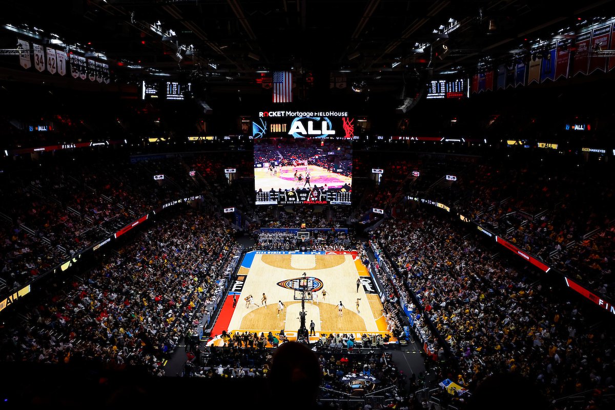 Crowded indoor basketball game at Rocket Mortgage FieldHouse with large overhead screen displaying players and audience filled with spectators.